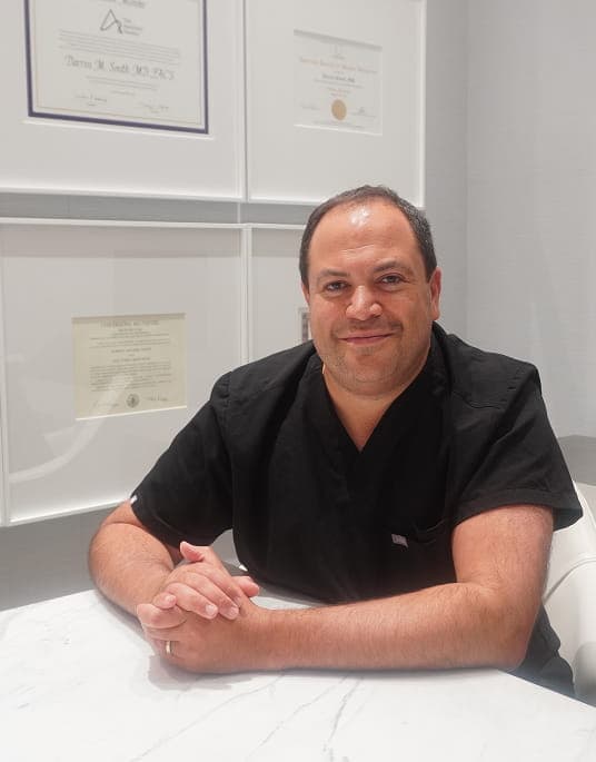 Dr. Darren Smith at marble table with framed certificates behind him