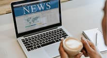 Laptop showing a news website beside a coffee cup.